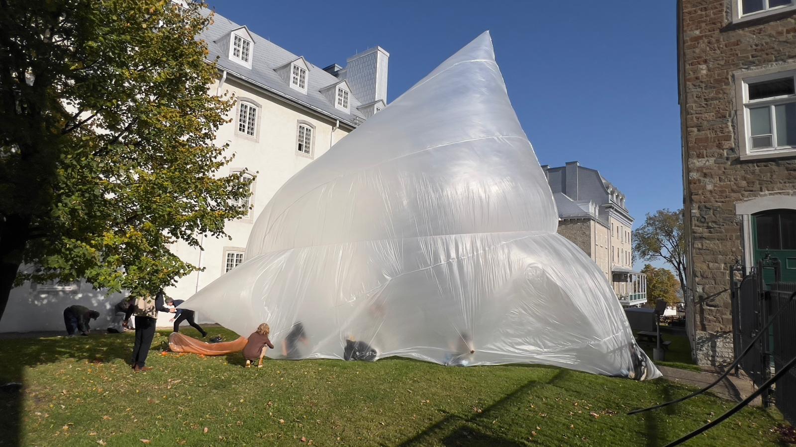Pavillon gonflable translucide dans une cour, avec plusieurs personnes autour de sa base.